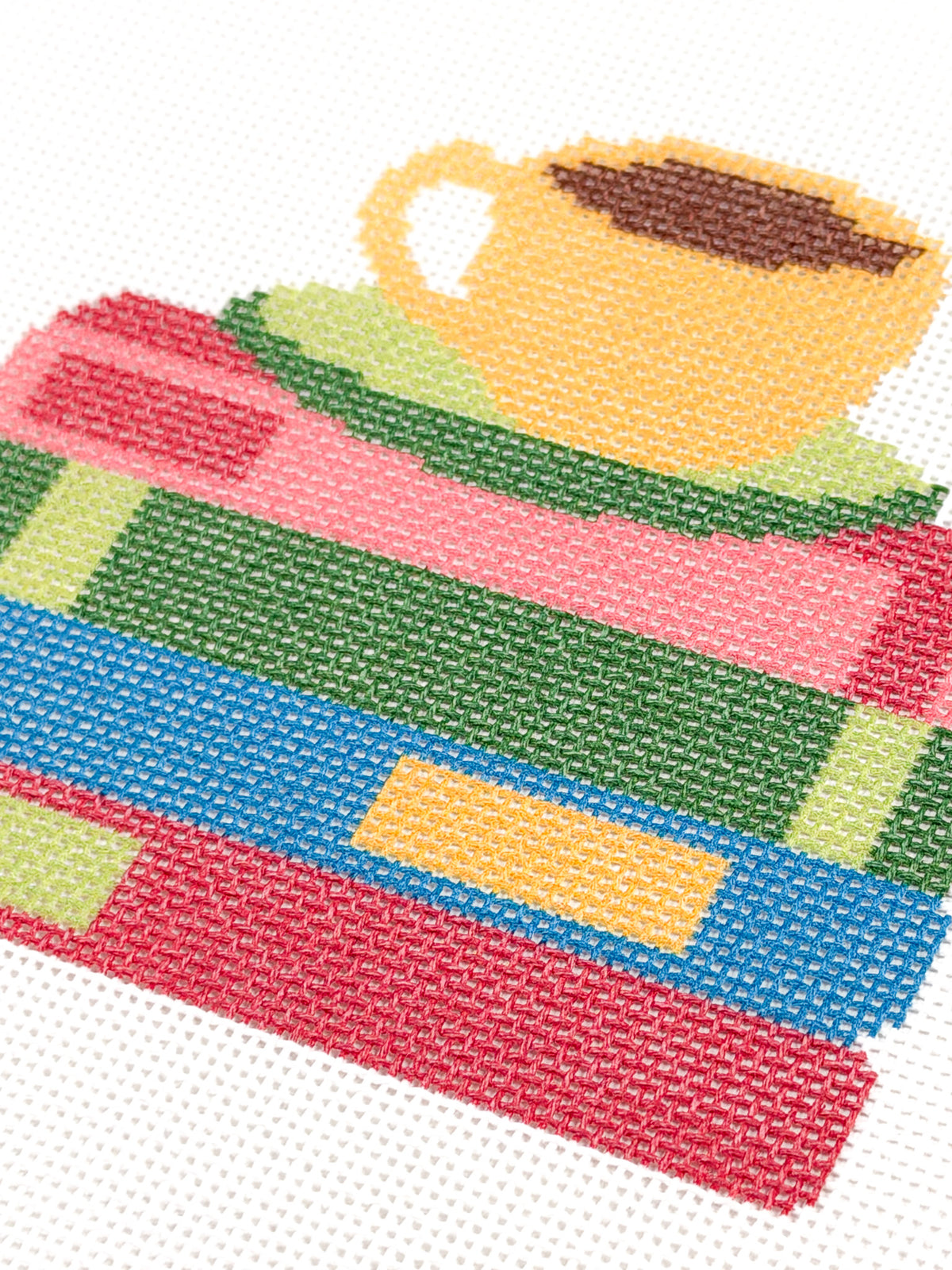 Close-up of the yellow coffee cup and colorful stacked books on Just One More Chapter needlepoint canvas.