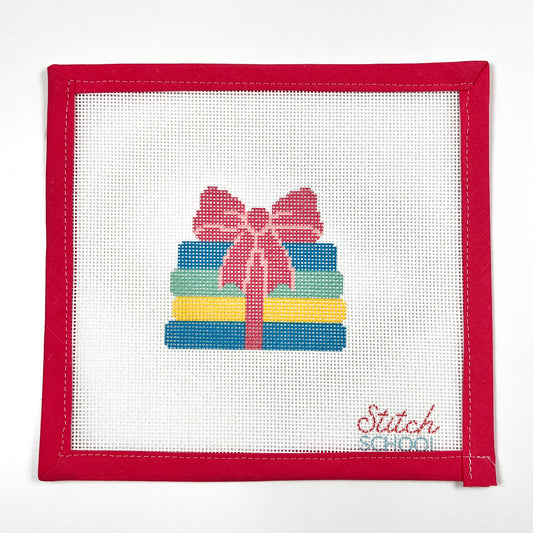 Books with a Bow needlepoint canvas with colorful stacked books tied with a pink bow, shown with red binding.