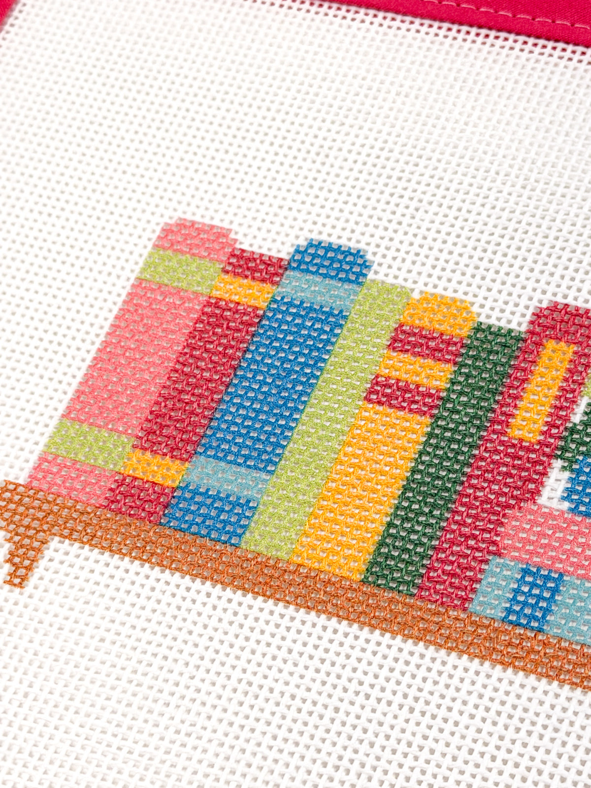 Close-up of colorful book spines and the brown shelf on Happy Little Bookshelf needlepoint canvas.