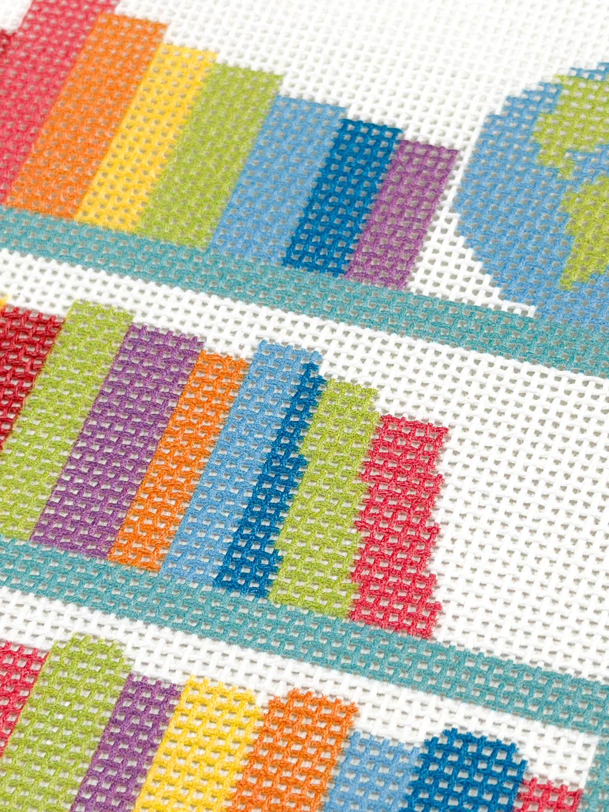 Close-up of rainbow-colored books on the teal shelves of Rainbow Library Cart needlepoint canvas.