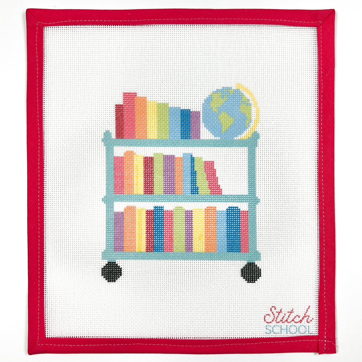 Rainbow Library Cart needlepoint canvas with a teal rolling cart, colorful books and a globe, shown with red binding.