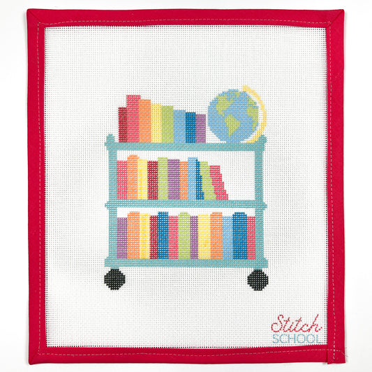 Rainbow Library Cart needlepoint canvas with a teal rolling cart, colorful books and a globe, shown with red binding.